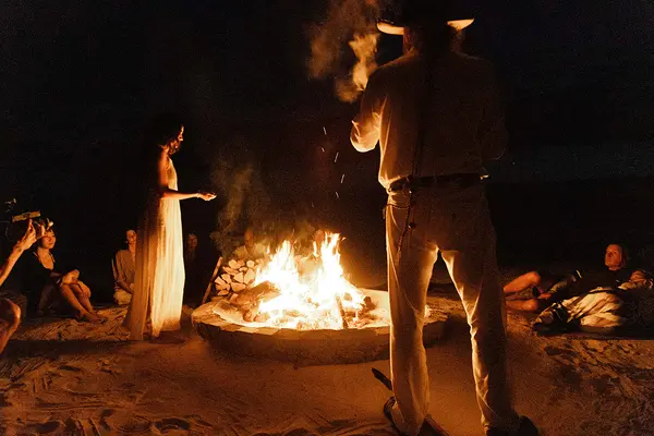 Grupo de personas reunidas alrededor de una fogata en la playa, bailando en Nômade Tulum, México.