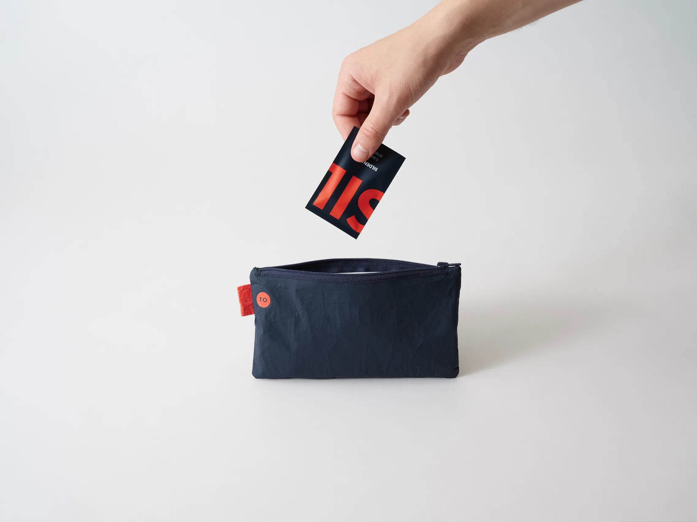 Hand placing a Ro medication packet into a black reusable pouch on a light background