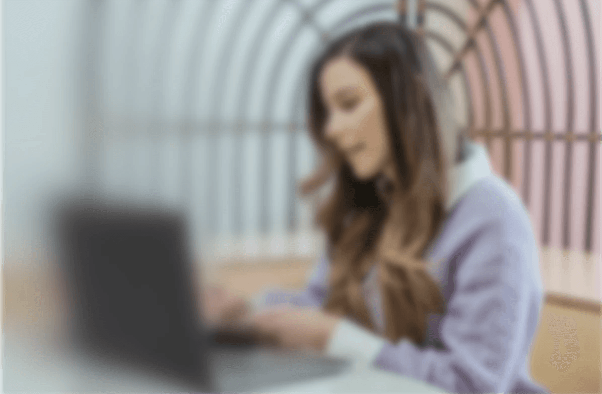Donna seduta a una scrivania lavora al computer portatile, in un ambiente luminoso con sfondo colorato e struttura ad arco.