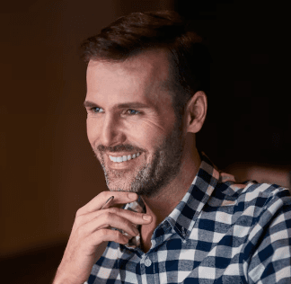 Moody portrait of a woman with straight dark hair and bangs leaning against a turquoise and pink wall, illuminated by soft natural light.