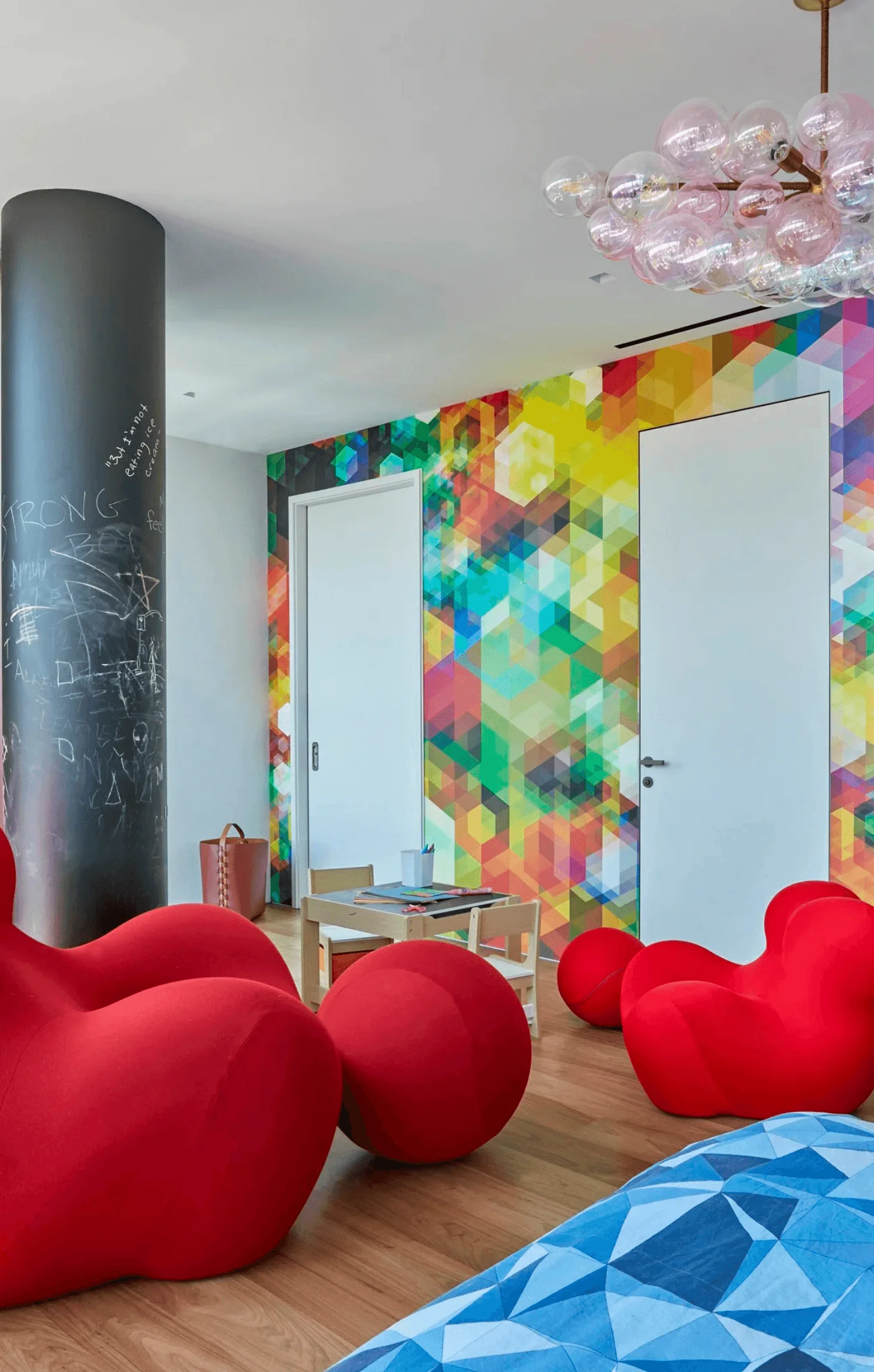 A playroom with a chalkboard column, red sculptural Up chairs, and a colorful geometric mural on the walls
