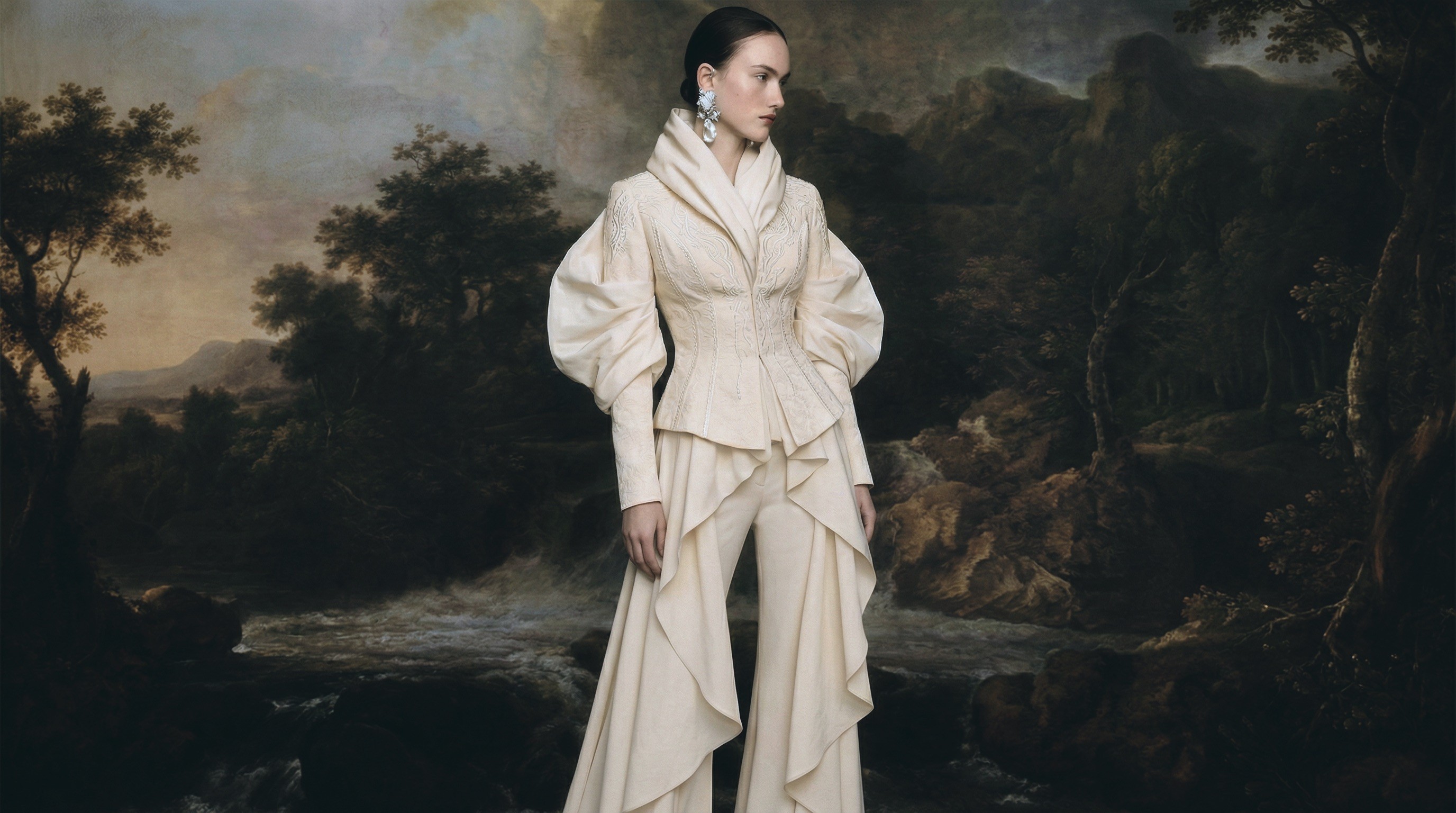 Powerful woman in a meticulous handcrafted embroidered ensemble standing in front of art piece.