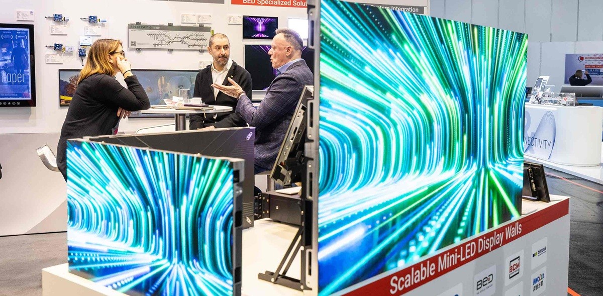 Attendees talk at an Embedded World expo booth showcasing scalable mini-LED display walls and e-paper display solutions, with bright LED panels in the foreground.