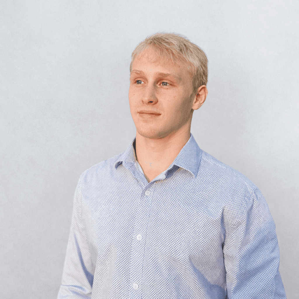 Professional headshot of a brunette woman in a white shirt, arms crossed, on a clean minimal background.