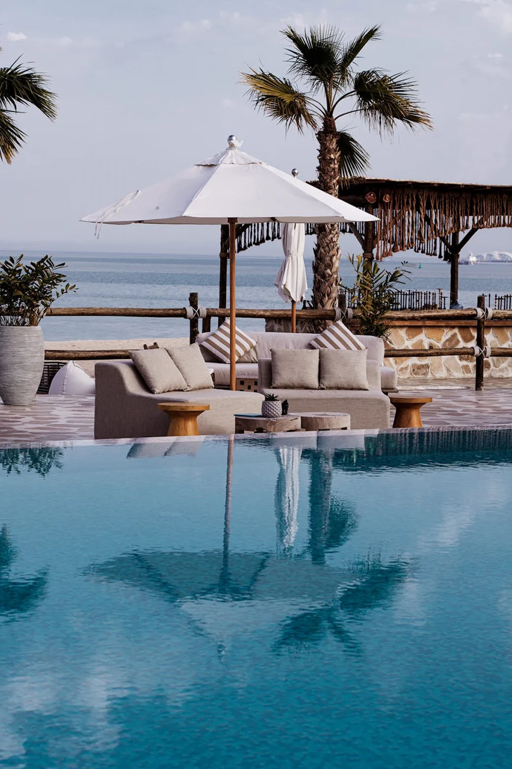 Poolside lounge chairs with a white umbrella overlooking the sea.