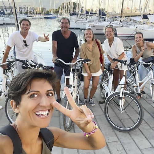 マリーナで数隻のヨットを背景に、6人のグループが自転車と共に笑顔でポーズを取っています。