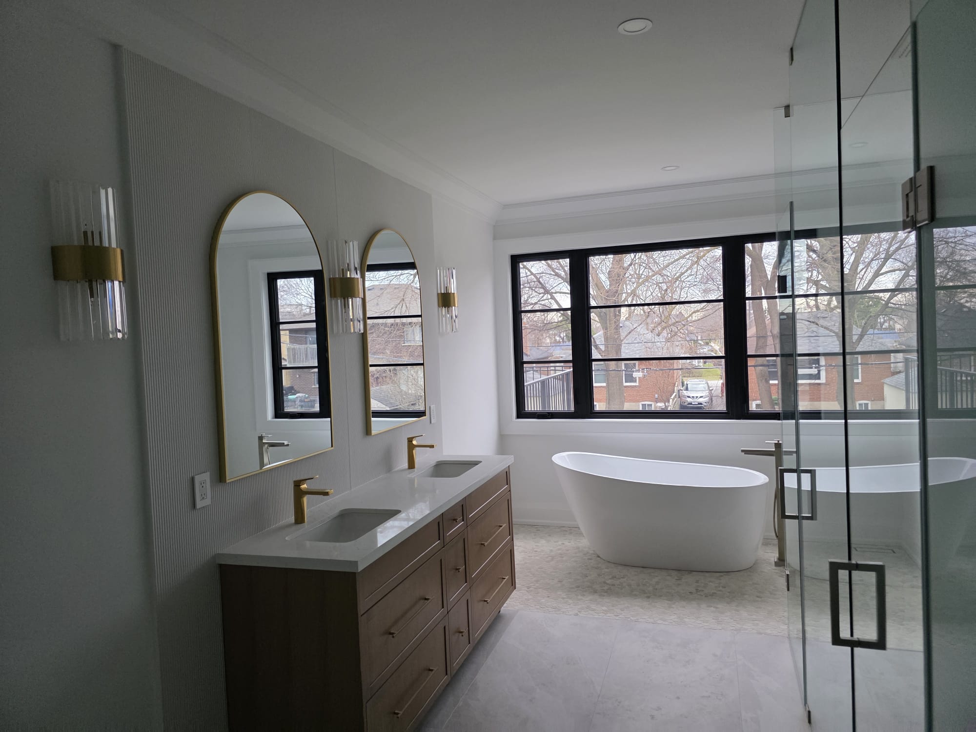 Modern two-story home with large glass windows, warmly lit interiors, and a balcony. Surrounded by trees and a manicured lawn at dusk. Cozy ambiance.