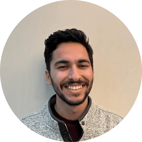 A person with wavy light hair stands facing slightly to the left, wearing a striped shirt against a neutral background.