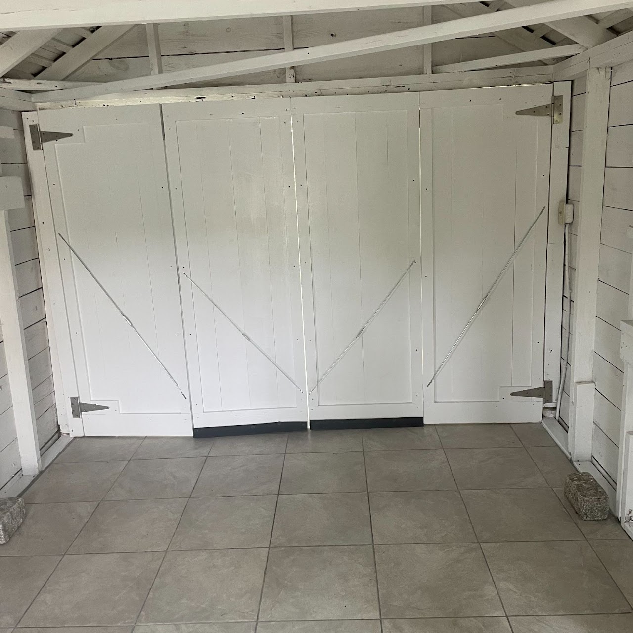 Interior of restored shed with white board doors over tile floor