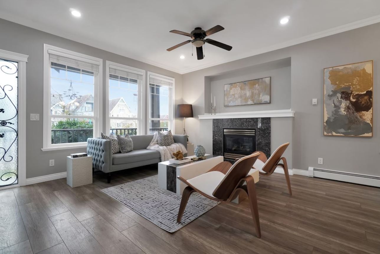 A modern living room with large windows, a fireplace, a ceiling fan, and stylish furniture.