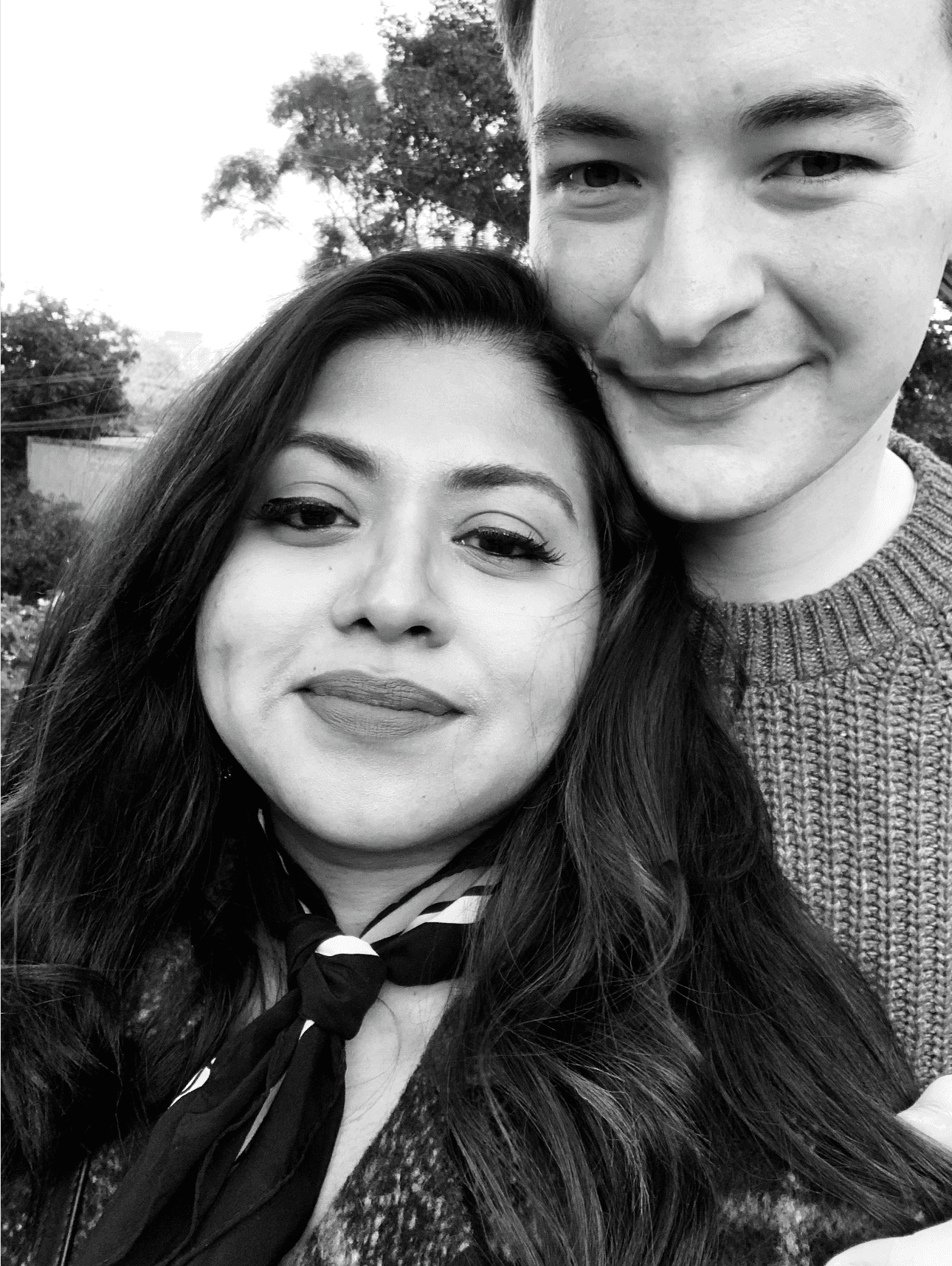 A woman with long blonde hair, in a brown top and jeans, walks through a sunlit forest, holding someone's hand. The scene is warm and inviting.