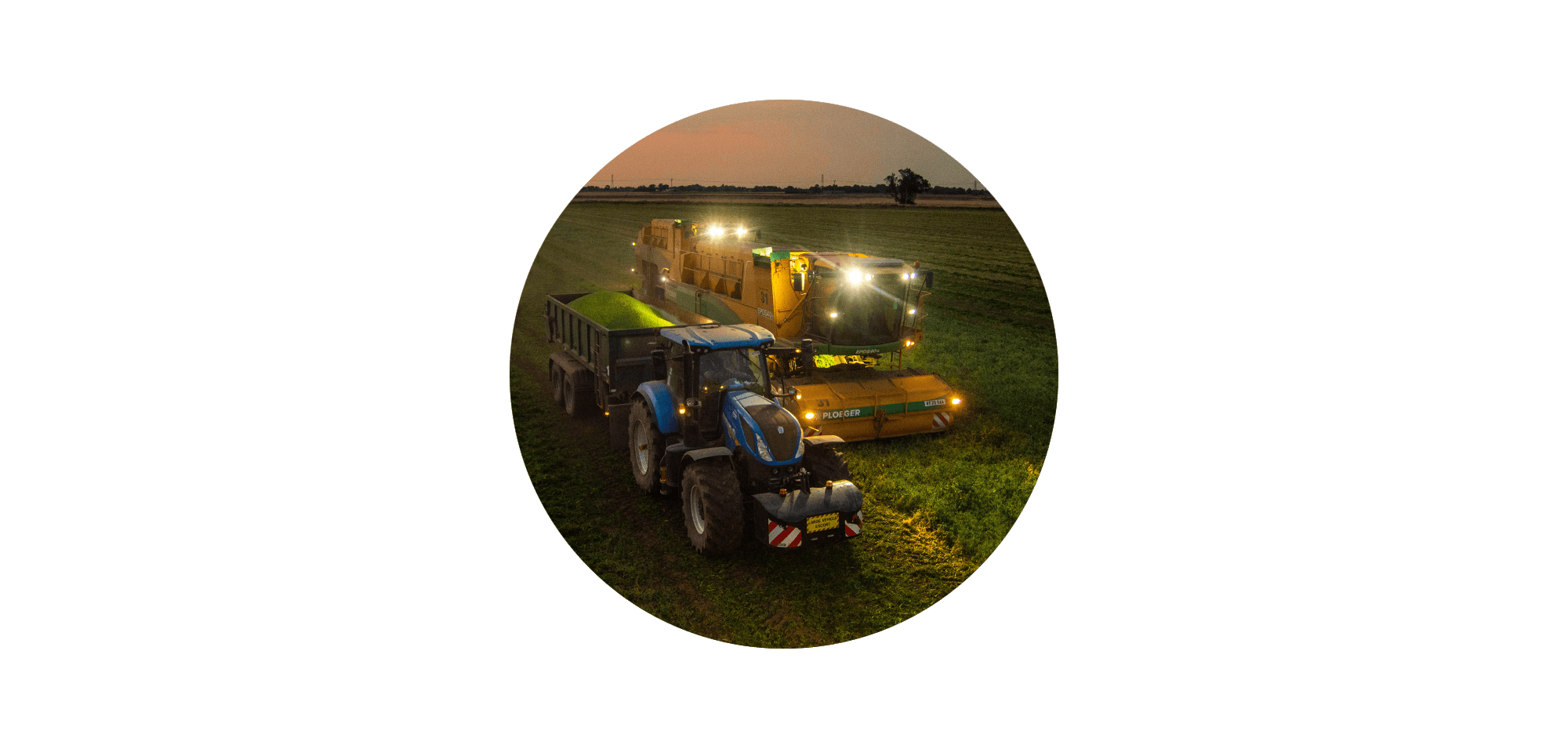 An aerial view of a Ploeger pea harvester and a blue New Holland tractor with a trailer full of freshly harvested peas, working together in a field at night under bright working lights, displayed in a circular crop against a black background.