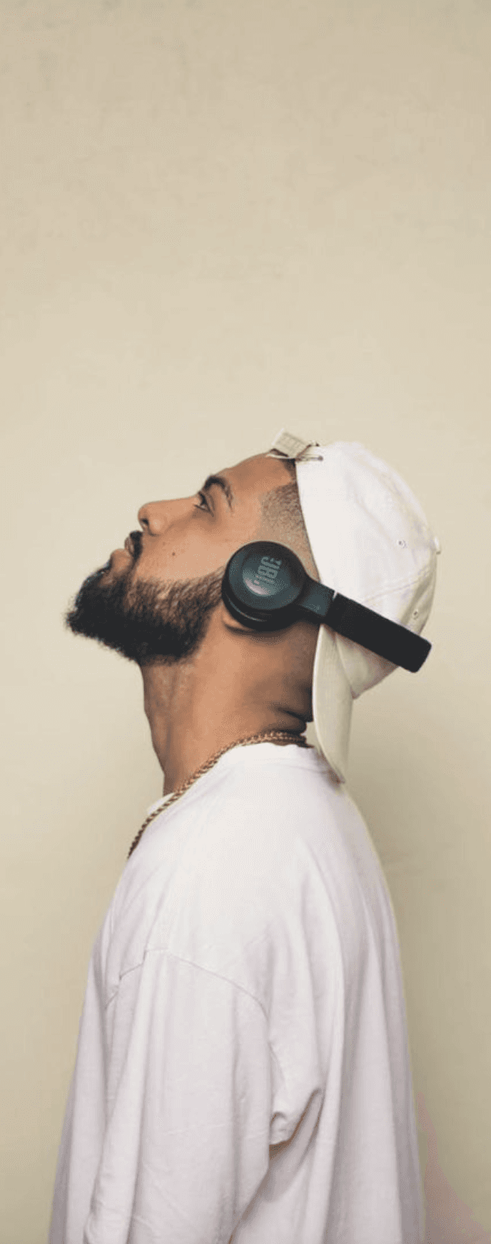 A person wearing headphones tilts their head back against a plain beige background.