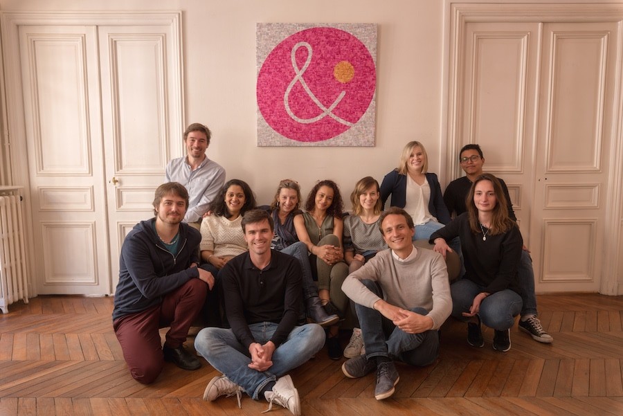 Photo de groupe de l'équipe Alenvi, assise et accroupie devant une œuvre en post-it rose