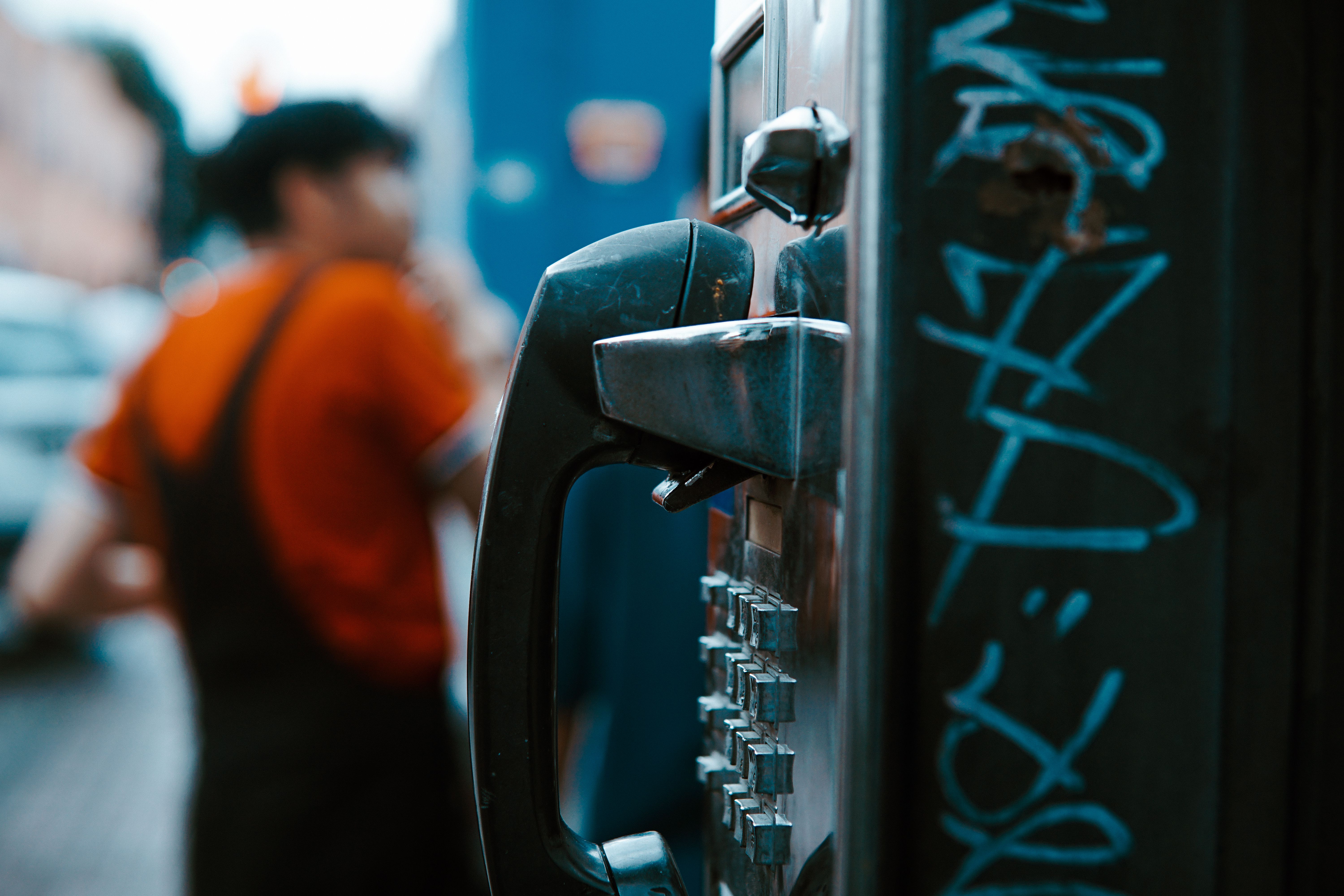 a close up photo of a telephone cabin and a man in the background, blurred with an orange t shirt and dungarees