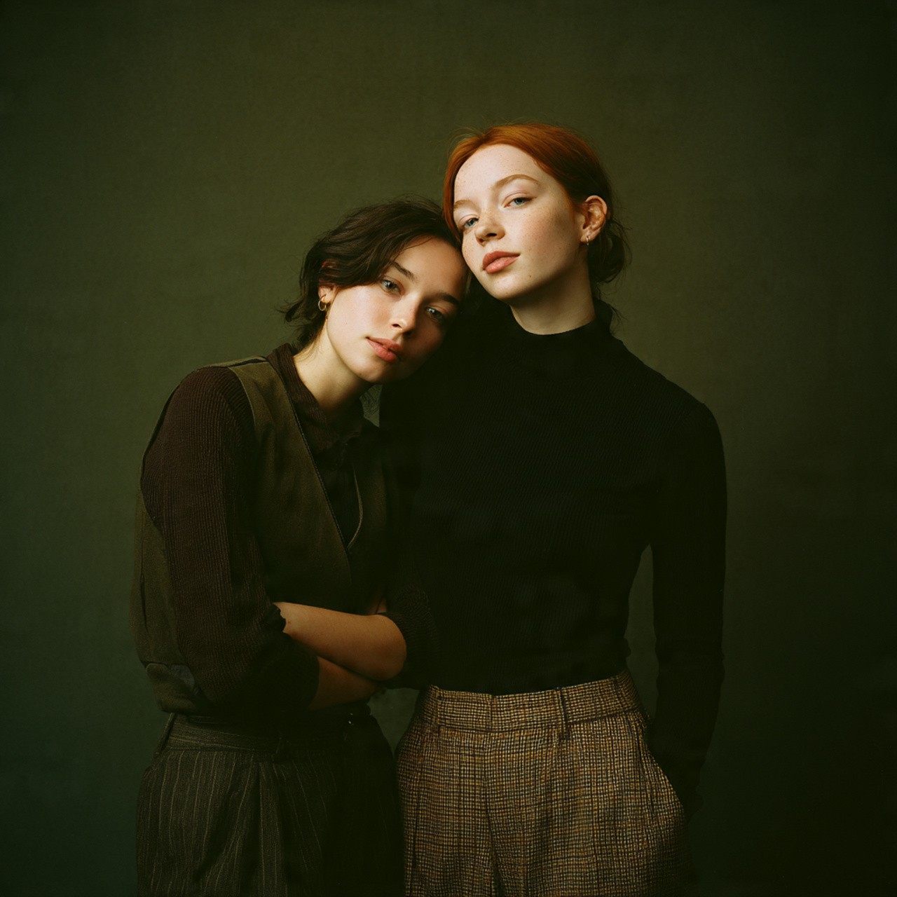 Two young women posing close together in muted, earthy tones.