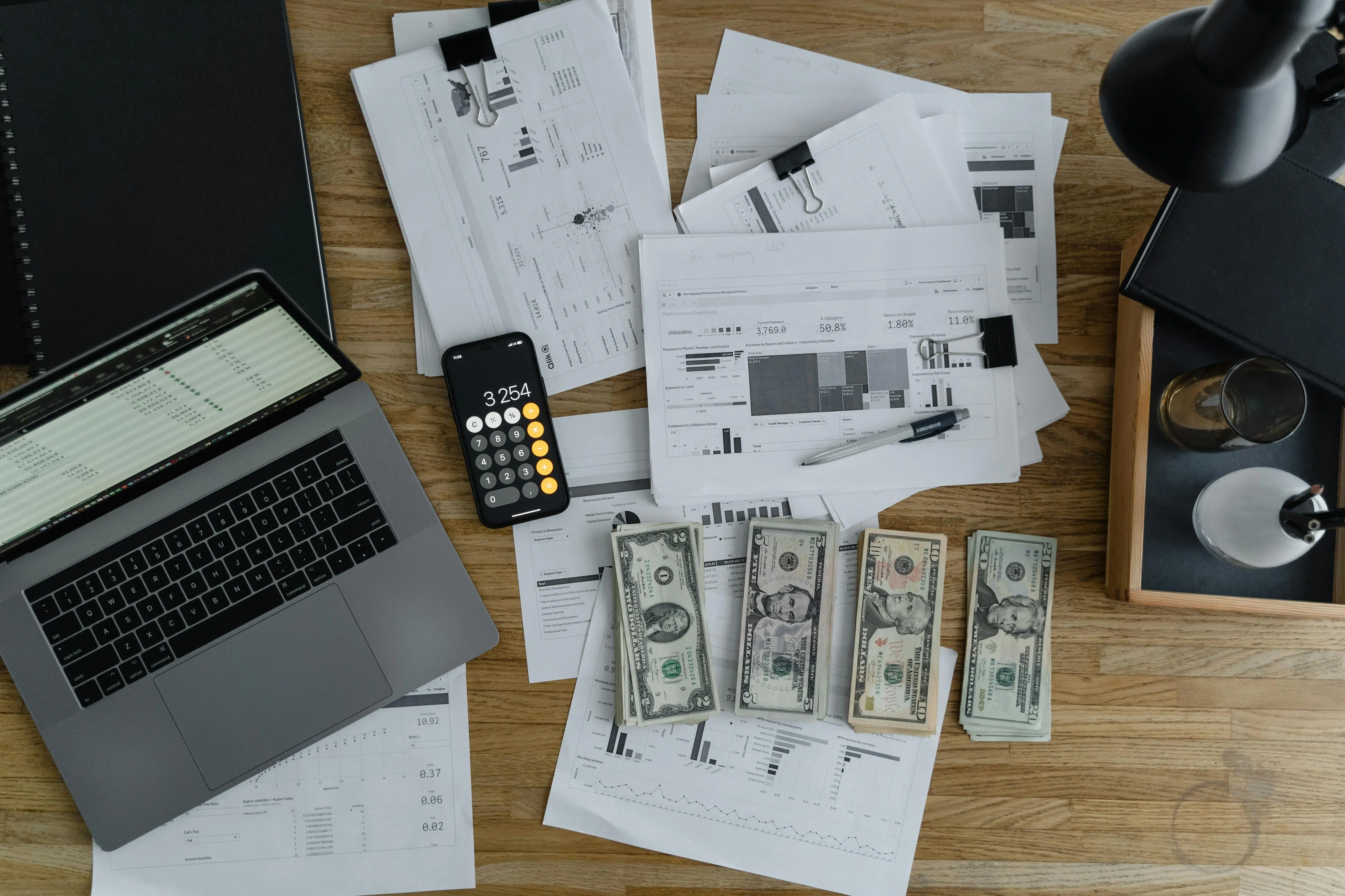 A top-down view of a desk with a laptop, calculator, cash, and financial documents