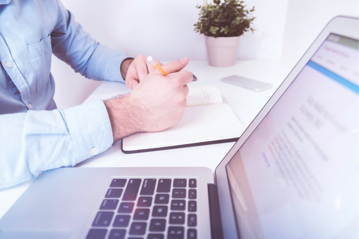 Man at laptop writing notes in office with desk plant