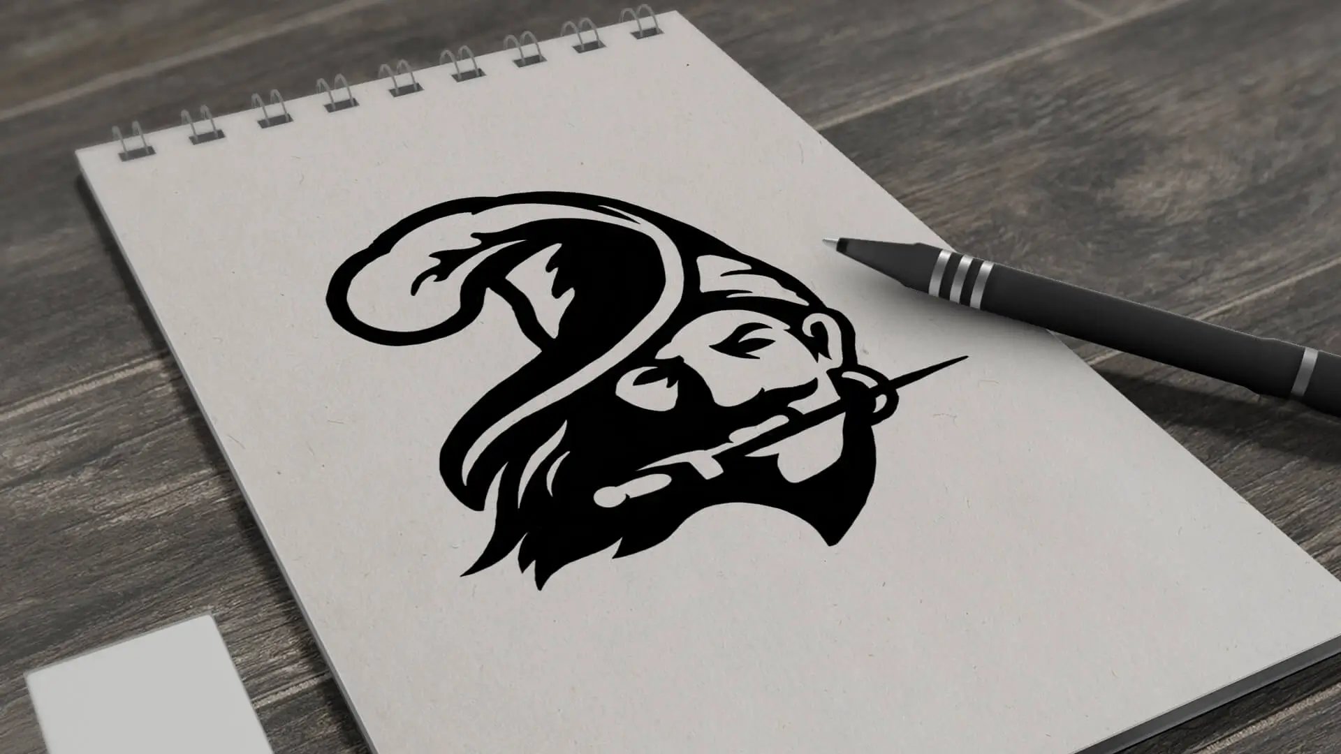 A sketch on a notebook shows a stylized face of a man with a bushy beard and hat. A pen lies beside it on a wooden surface, suggesting creativity.