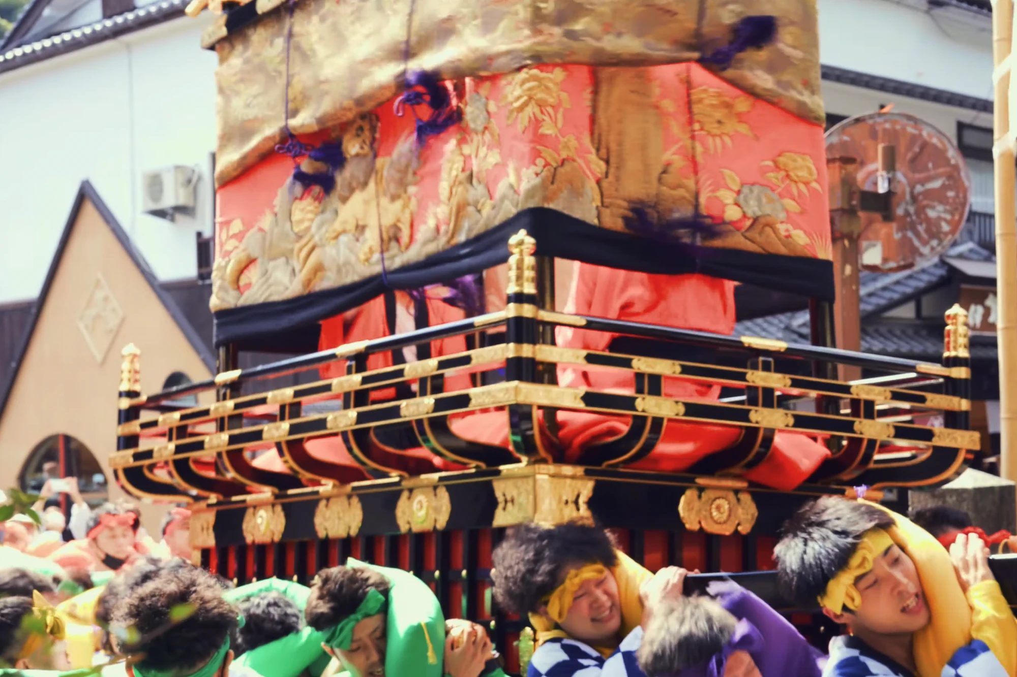 A gilded festival float carried shoulder-high through a Kinosaki street by bearers in happi coats.