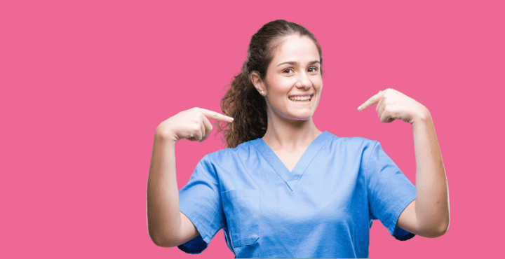Smiling healthcare worker in scrubs pointing at herself on a pink background