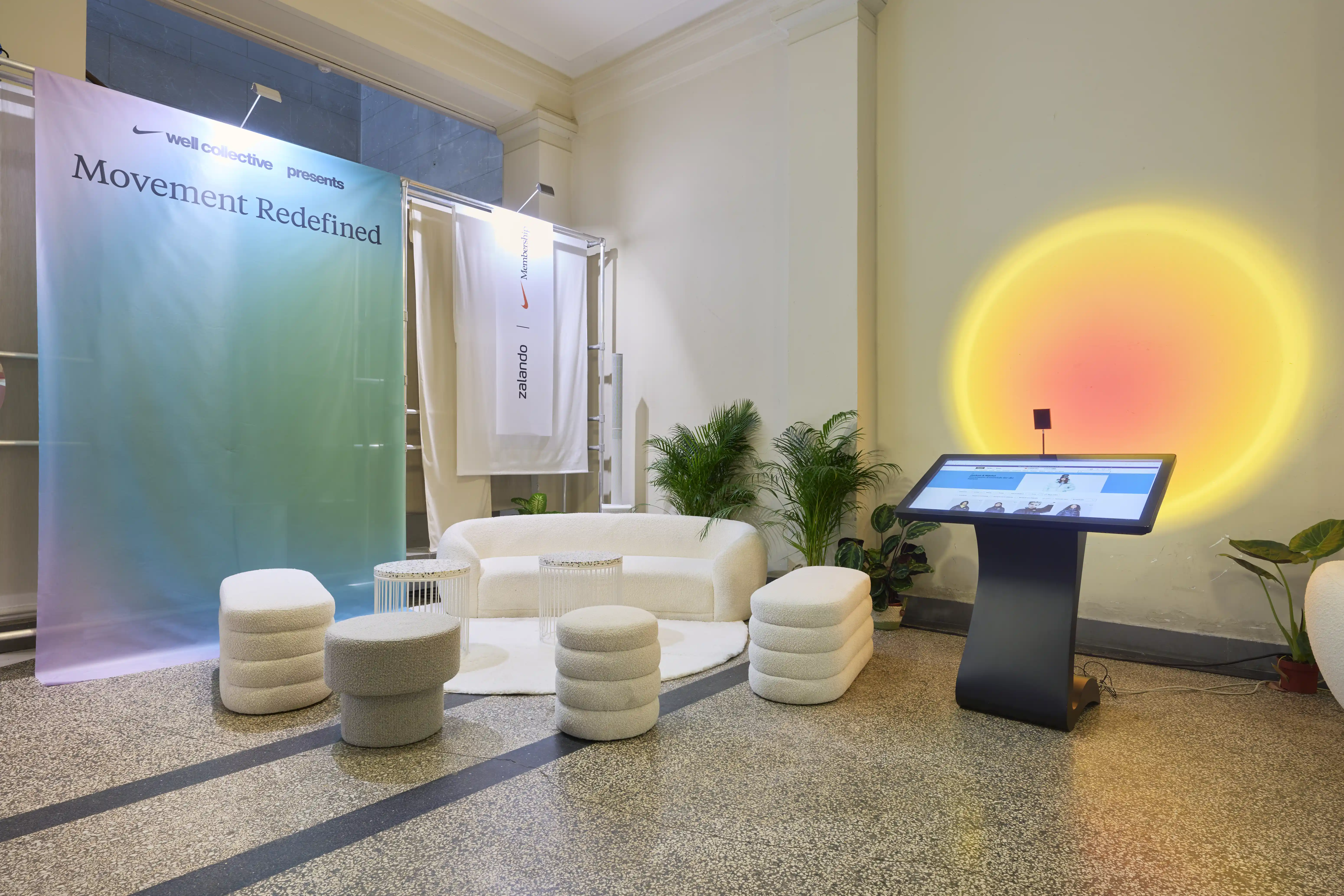 Lounge corner with gradient Movement Redefined banner, white sofa, poufs and interactive screen.