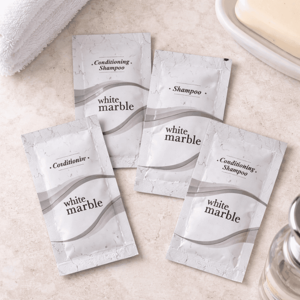 White Marble hotel amenity sachets including shampoo, conditioner, conditioning shampoo and lotion arranged on a bathroom countertop in top view, by Transmacro Amenities