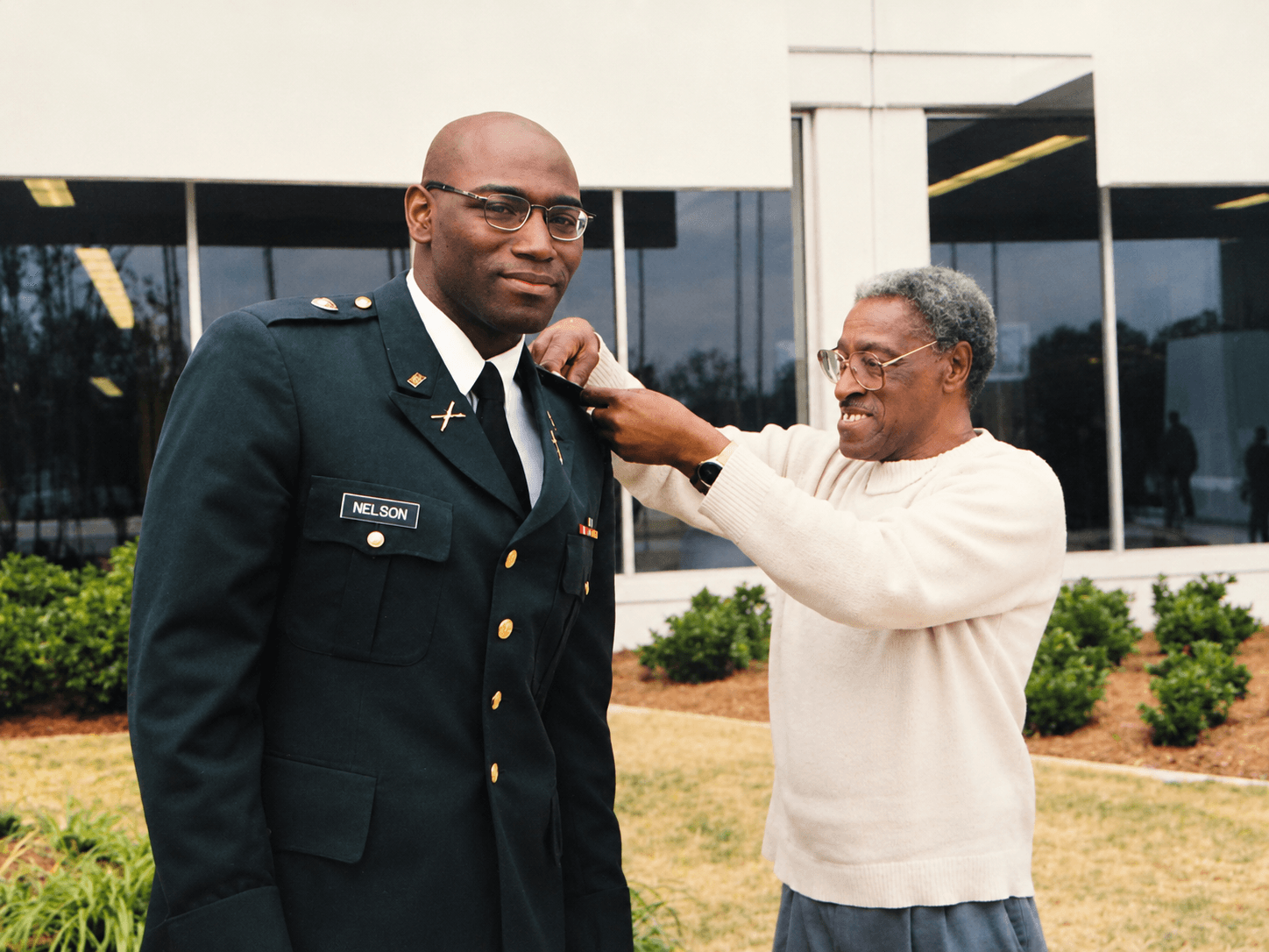 Brad D. Nelson in military uniform as an older man adjusts his shoulder insignia.
