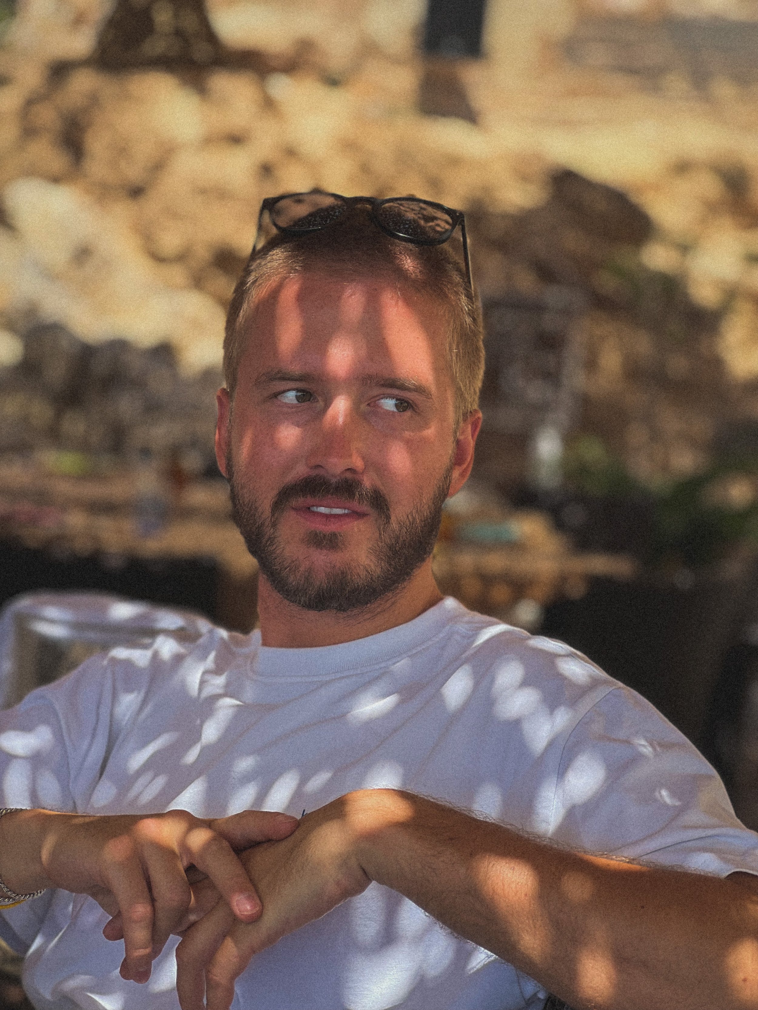 Adam Kaiser outdoors in sunlight, wearing a white T-shirt with glasses resting on his head.