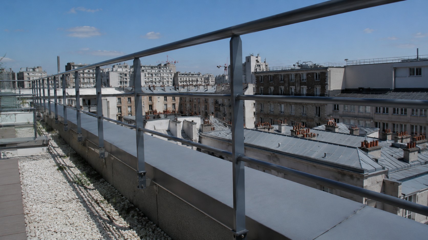 Garde-corps métallique conforme sur toiture-terrasse à Paris, avec fixation sur acrotère, lisses de protection et vue sur les toits parisiens, illustration de la norme NF E 85-015 pour la sécurité en hauteur.