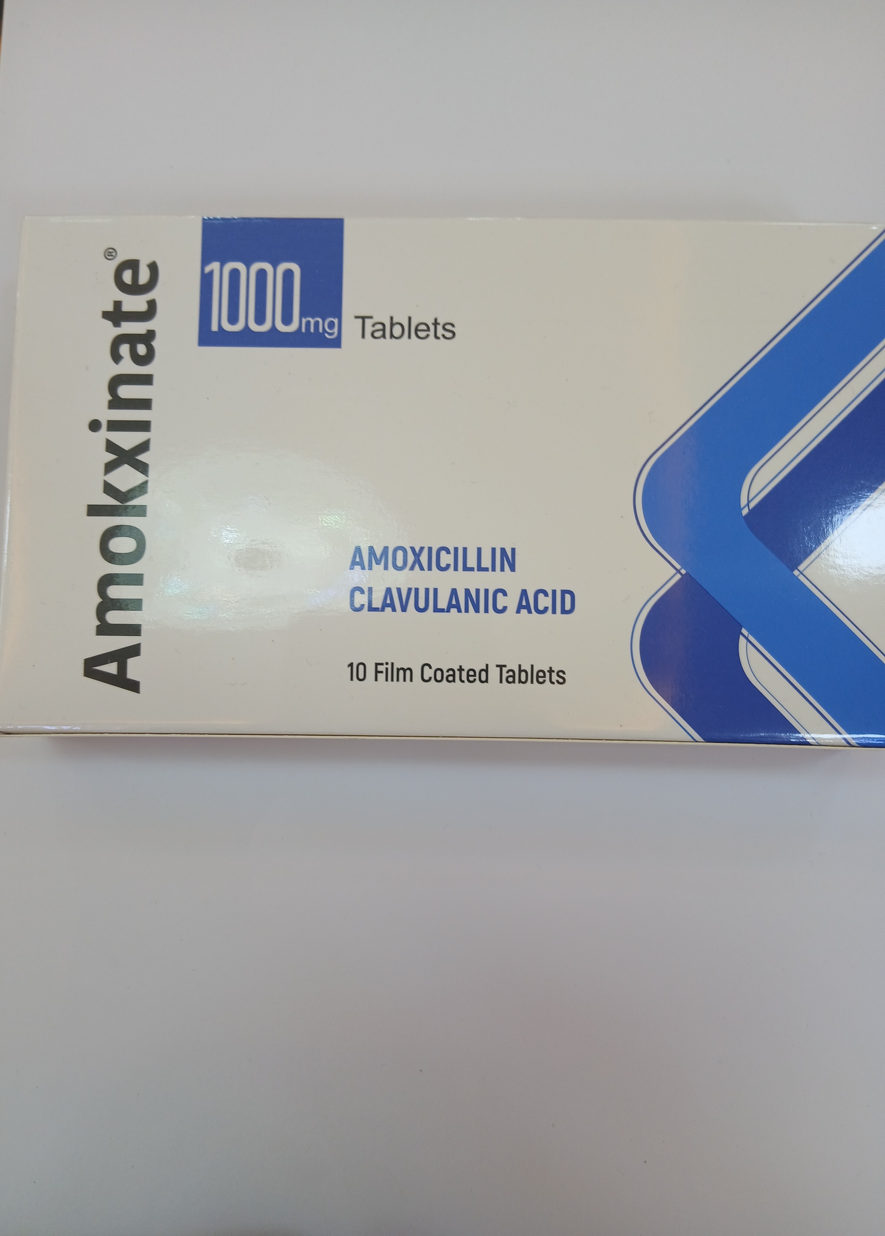 White cardboard box packaging displays blue text and graphics, indicating it contains 10 film-coated tablets of 1000 mg each.