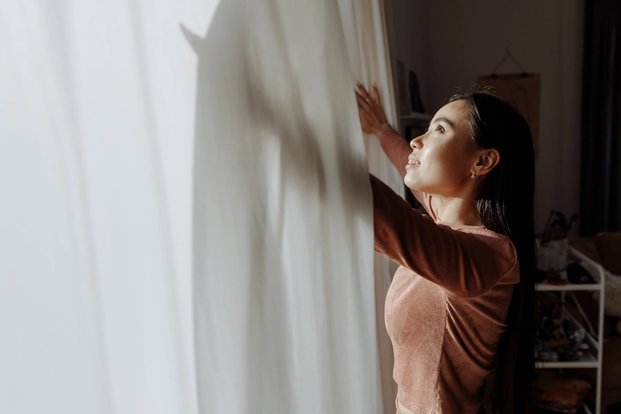 A woman opens the blinds on a window