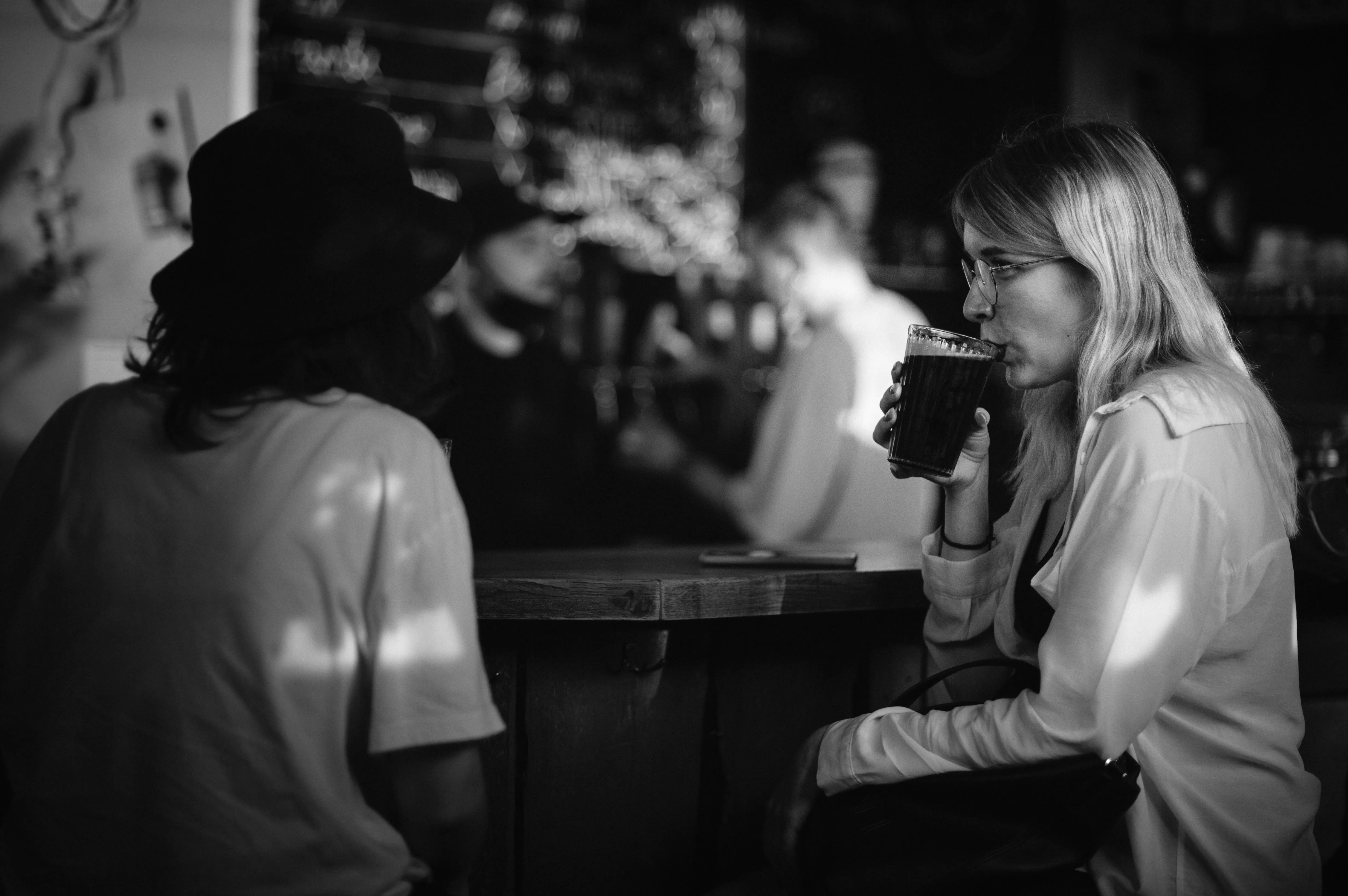 Two people in a dimly lit setting, engaged in conversation, with a blurred background of others.