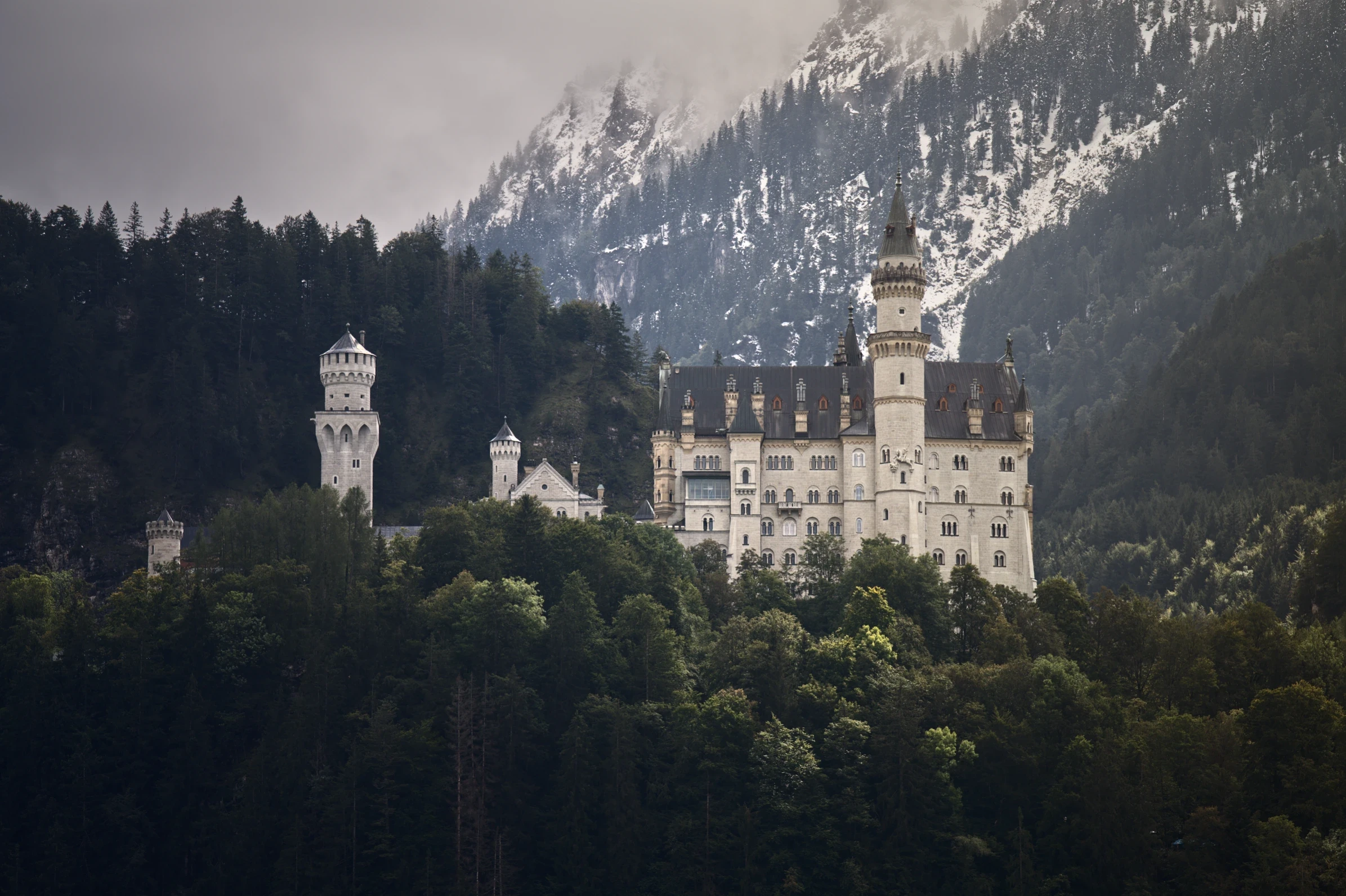 Schloss Neuschwanstein eingebettet in die alpine Landschaft mit schneebedeckten Bergen im Hintergrund.