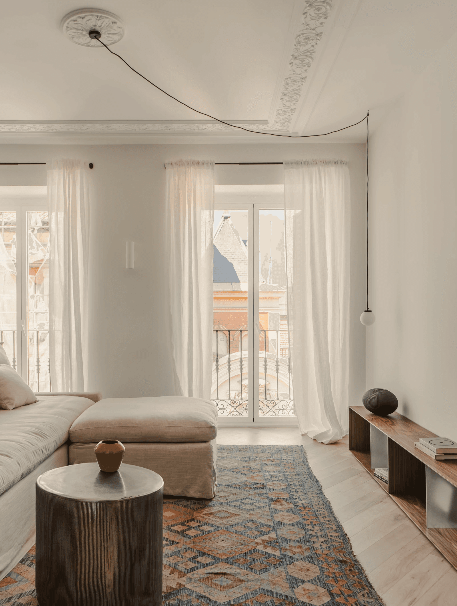 Living room with balcony, vintage rug and lounge chair in a Madrid home by Atrato Estudio