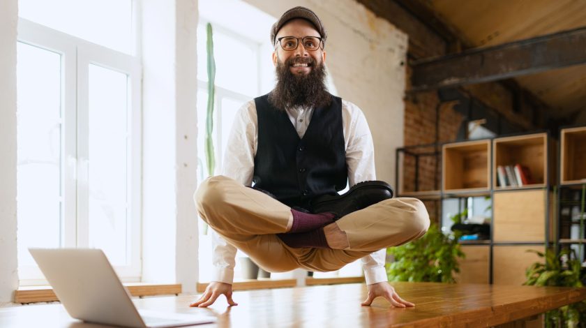 A person is meditating in a seated position, levitating above a table in a bright, modern room.