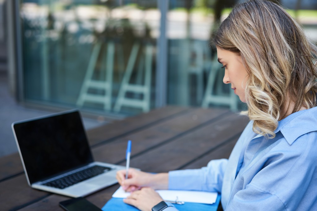 Person writing in front of a laptop, organizing what documents should you bring to an interview for a polished and professional impression.