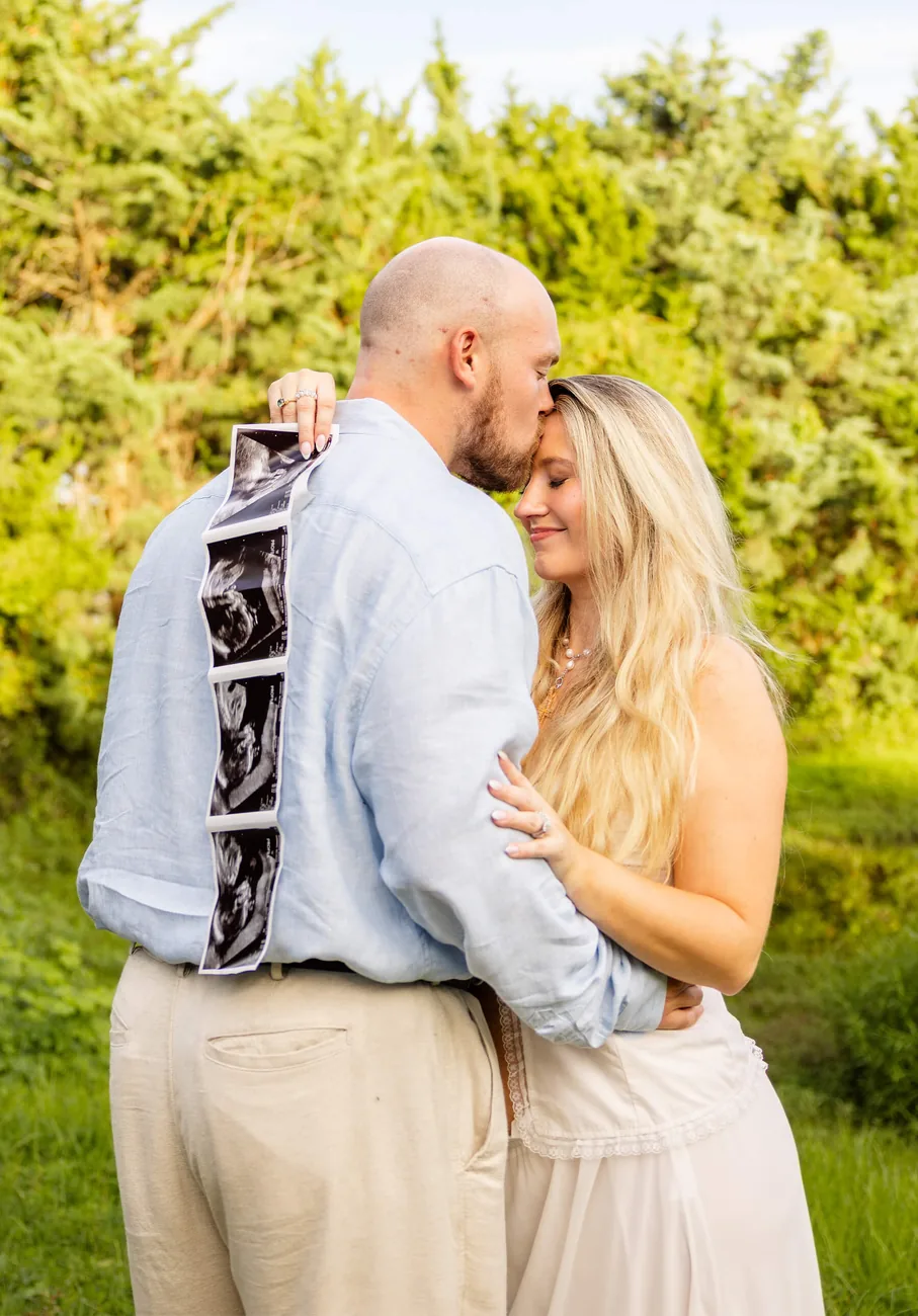 Expecting couple embracing while holding a strip of ultrasound photos, by Sioux Falls, SD maternity photographer Kelsey Lynn