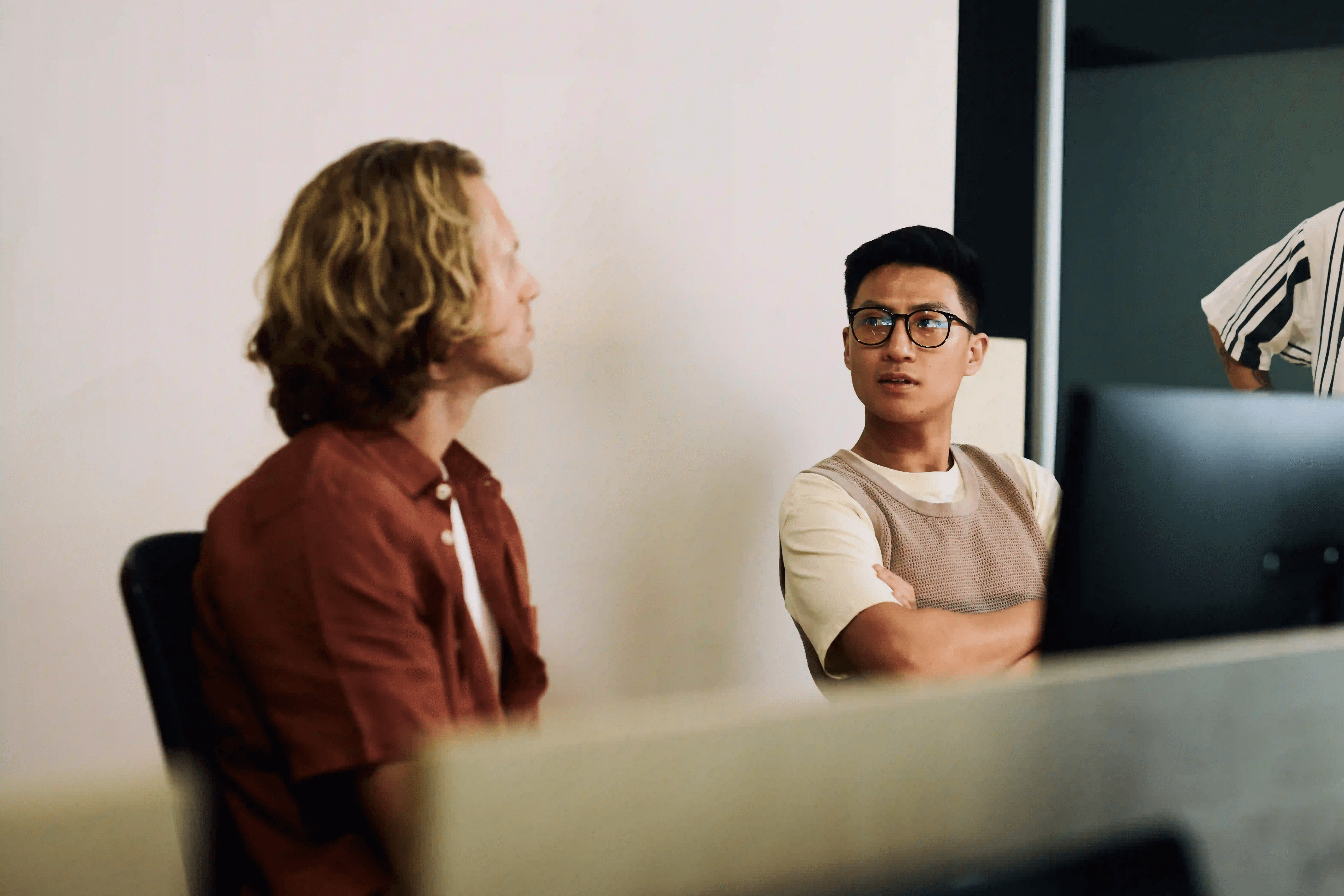 Close-up of a large, structured brown leather tote bag held by a person in a belted khaki trench coat, shown against a textured natural backdrop.