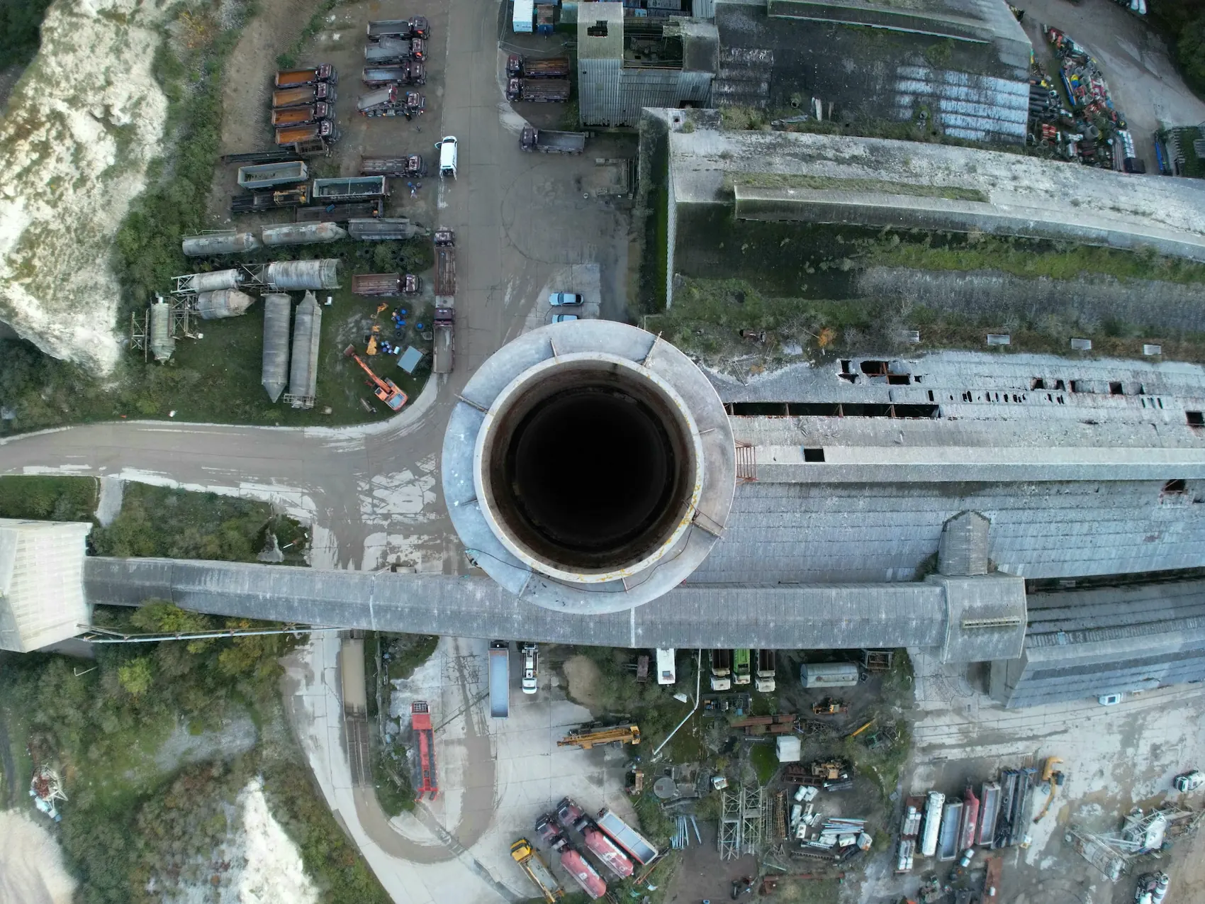 Top-down aerial drone photography looking directly into an industrial chimney opening surrounded by a factory site