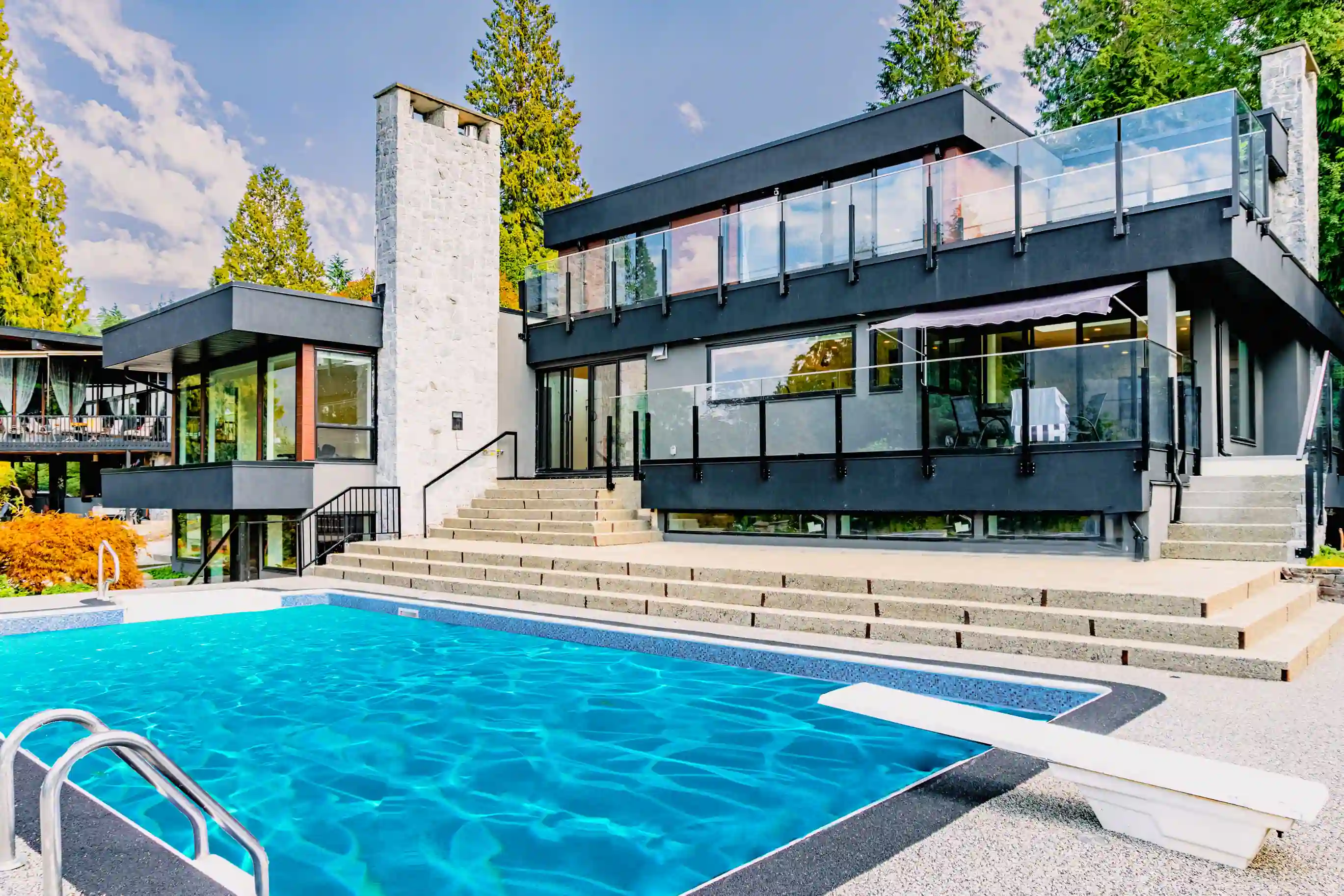 Modern custom home exterior with glass railings, terraces, and outdoor pool