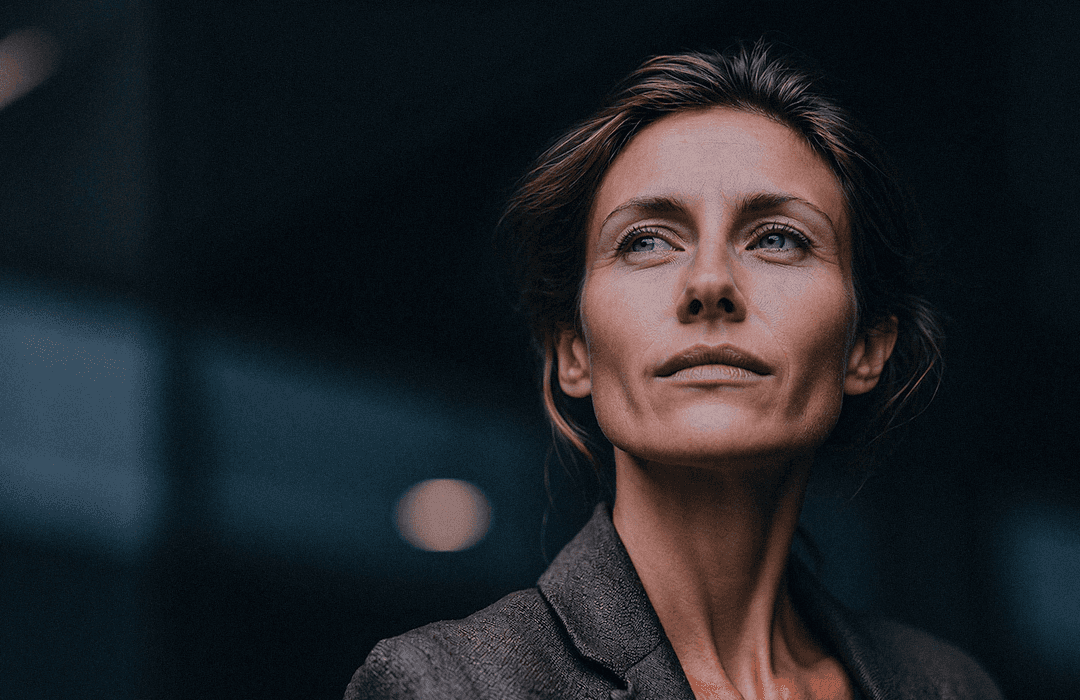 Close-up de mulher com olhar focado e determinado em fundo urbano desfocado.