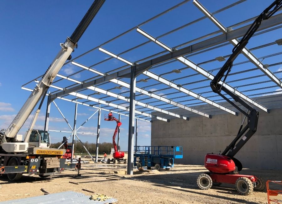 Grue soulevant une poutre métallique pendant la phase d’assemblage de la charpente.