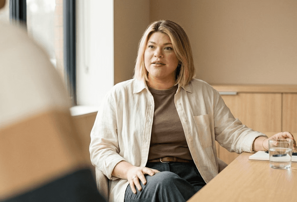 Woman in a light overshirt seated at a table during a meeting