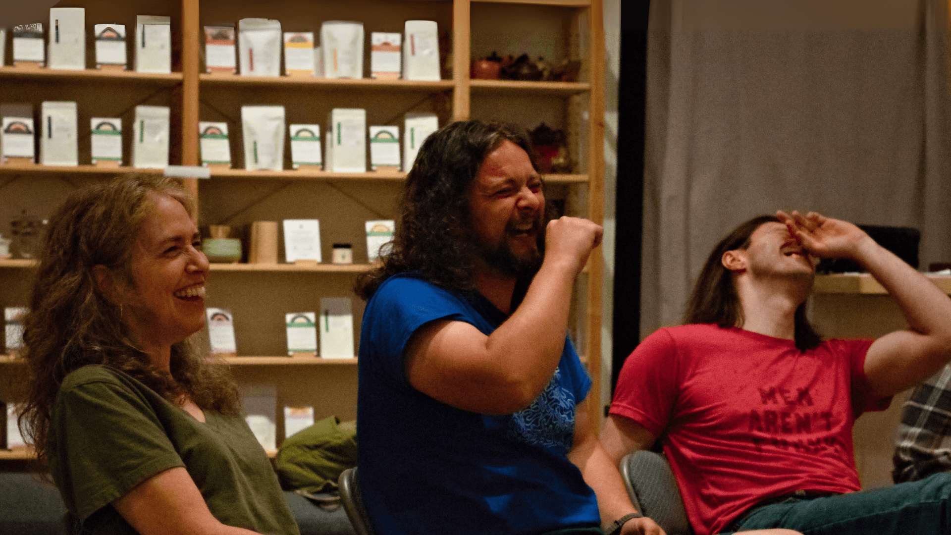A group of people in a room, one person in focus is laughing, set in a cozy environment with soft lighting and artwork on the walls, creating a lively mood in an Improv class with Black Sheep Comedy in Chapel Hill and Carrboro