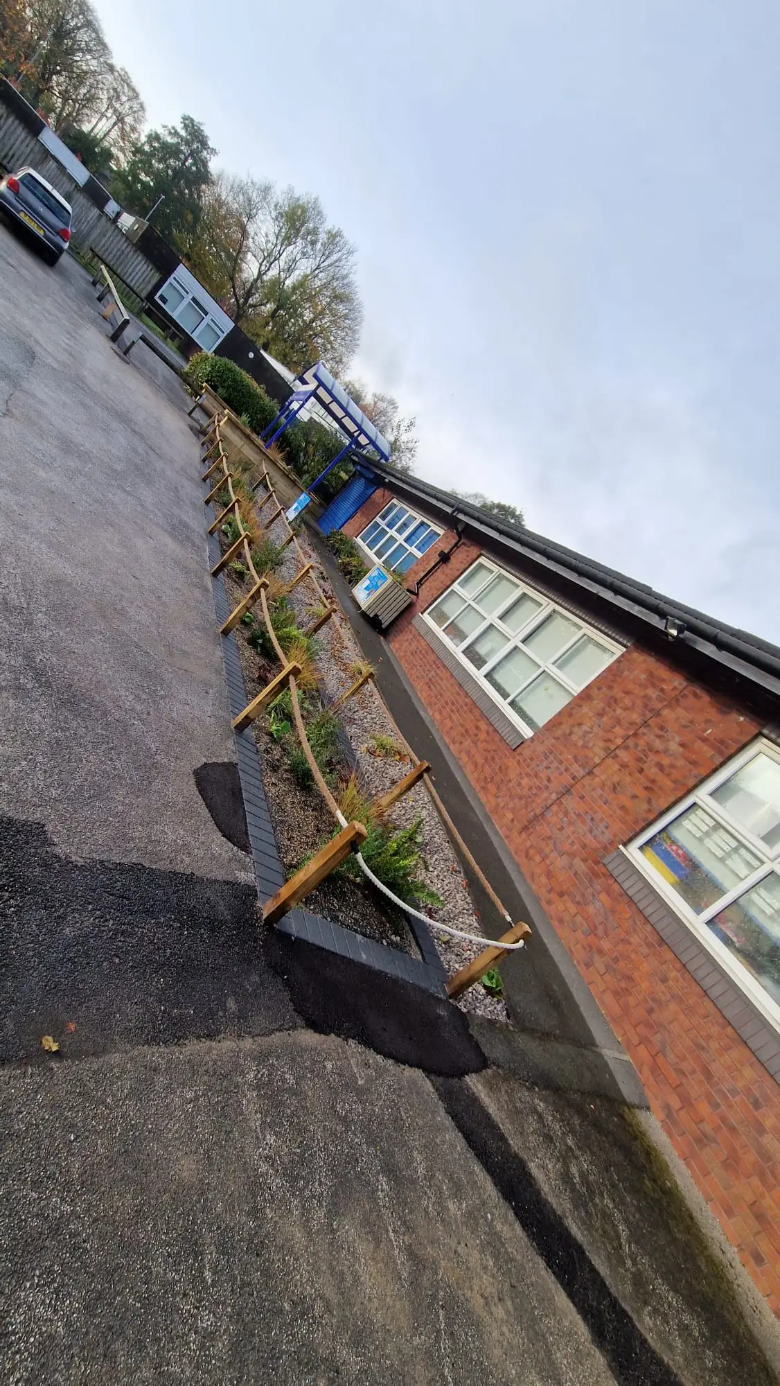 A sloped view of a street with a brick building and colorful flowers along the sidewalk under a clear sky.