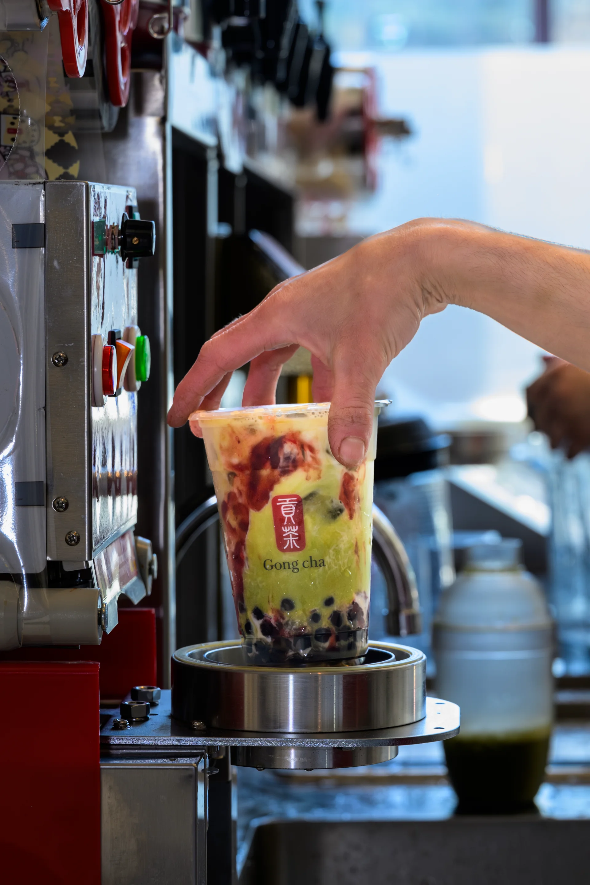 Barista sealing a Gong Cha bubble tea with tapioca pearls and fruit at the shop counter