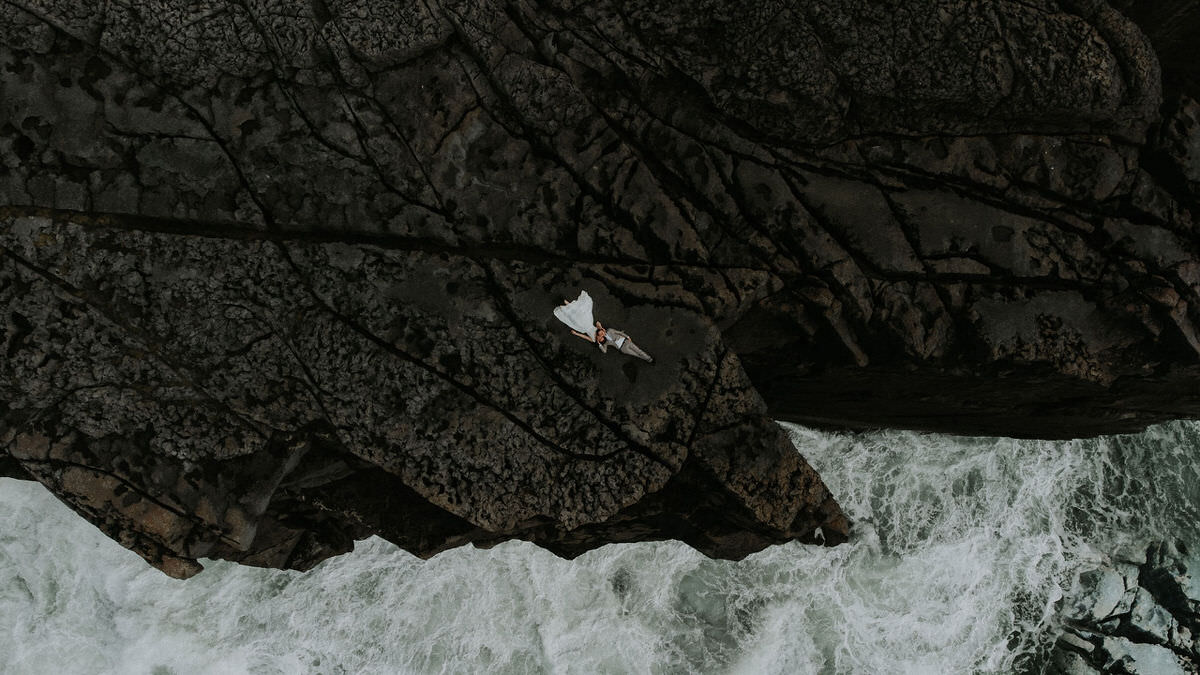 drone shot from above with elopement couple lying on rock formations with water below