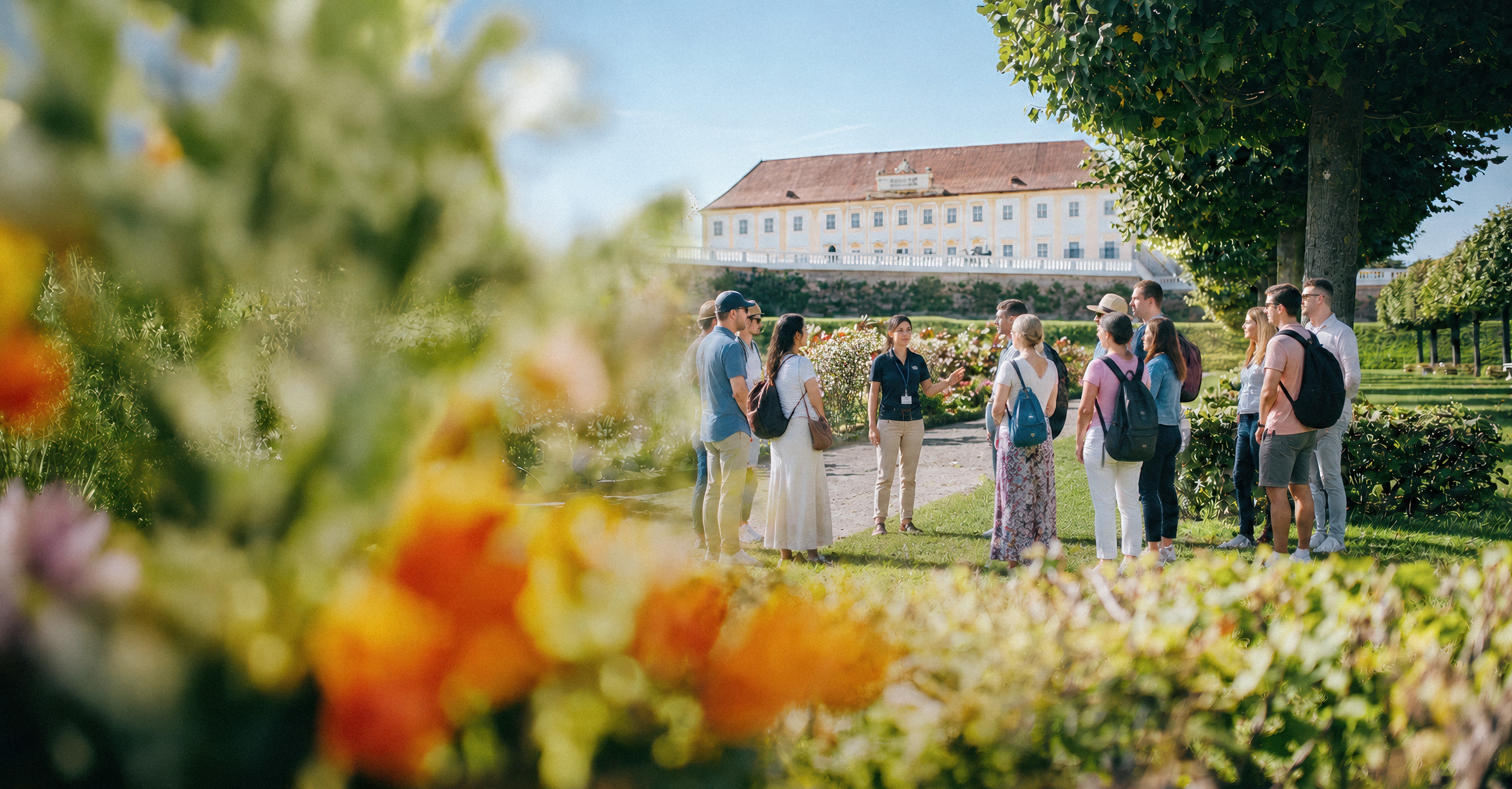 Gruppe von Besucherinnen und Besuchern im Garten vor einem barocken Schloss