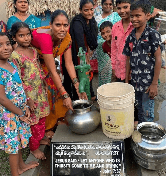 Women and children gather around a hand pump in a rural village, collecting clean water provided through a nonprofit initiative initiative.